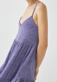 Violet slip dress with thin straps, V-neckline, and textured fabric featuring white spots. The skirt is flared with gathered details.
