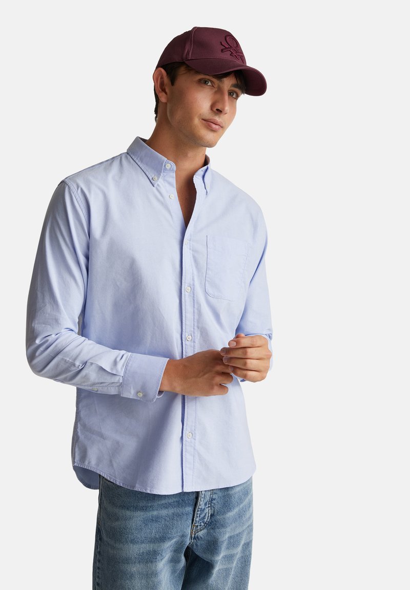 Modrá košile s knoflíky, která má malou náprsní kapsu, je vyrobena z bavlny a má dlouhé rukávy. Spodní část je doplněna o vínovou baseballovou čepici.