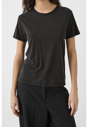 Woman wearing a plain black short-sleeve crew neck t-shirt and black pants, standing with arms relaxed by sides.