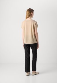 Beige T-shirt met korte mouwen en een relaxte pasvorm, gecombineerd met zwarte broek en lichtbeige platte schoenen, met een eenvoudige, minimalistische uitstraling.
