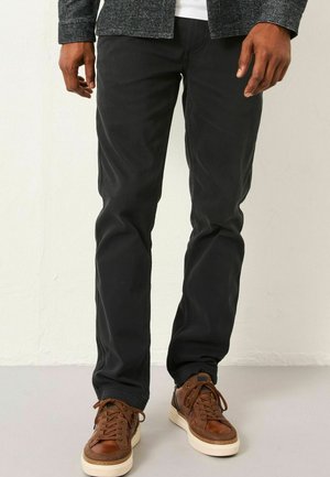 Black denim jeans with a slim fit, paired with brown leather sneakers featuring white soles and laces. Texture appears smooth and durable.