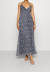 Maxi-jurk met een smock-borstvoeding in donkerblauw, met een bloemenpatroon in roze en groen. Dunne verstelbare bandjes en een vloeiende silhouet.