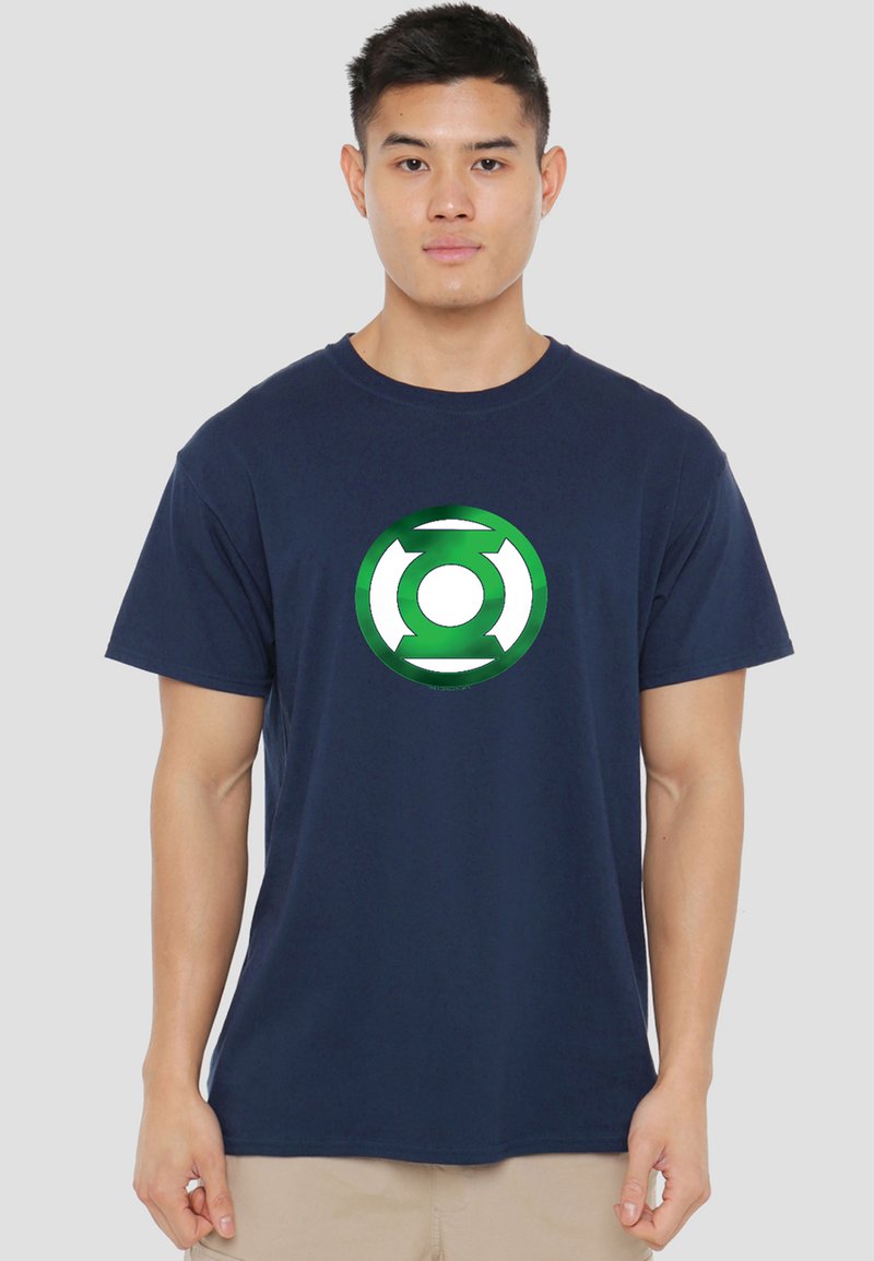 Young man wearing a navy blue T-shirt with a green and white Green Lantern logo, standing against a plain light gray background.