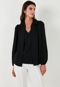 Black blouse with a collared design, billowy sleeves, and a button front. Features a smooth texture and a layered, v-neck style underneath.