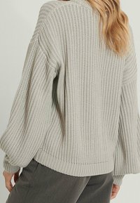 Maglione grigio chiaro lavorato a maglia con texture a costine, maniche ampie e vestibilità rilassata. Presenta un collo rotondo e dettagli a costine sull'orlo.