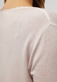 Haut rose pâle à manches courtes avec une texture lisse, un col rond et des coutures arrondies aux épaules. Les détails des coutures sont subtils et raffinés.