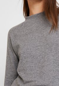 Szary sweter z okrągłym dekoltem, prążkowany, o miękkiej fakturze i rękawach raglanowych. Tkanina wydaje się nieco puszysta i lekka.