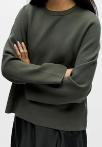 Oliwkowy sweter z okrągłym dekoltem, opadającymi szwami na ramionach i luźnym krojem, wykonany z miękkiego materiału o gładkiej strukturze.