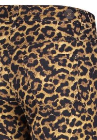 Jeans con estampado de leopardo sobre un fondo oscuro y manchas marrones. Presentan bolsillos traseros y una etiqueta en la cintura con el logo "Dream Jeans". Textura suave.