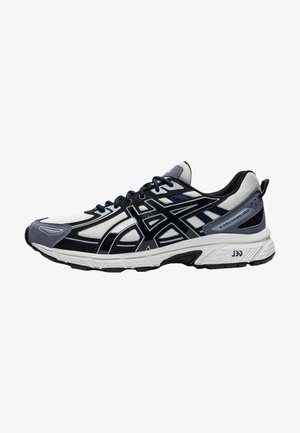 Zapatilla de running en negro, gris y blanco con parte superior de malla, detalles texturizados y suela acolchada. Cuenta con cordones y marca en el lateral.