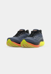 Zapatillas deportivas azules con acentos negros, suelas amarillas brillantes y detalles naranjas. Cuentan con una parte superior transpirable y una suela texturizada.