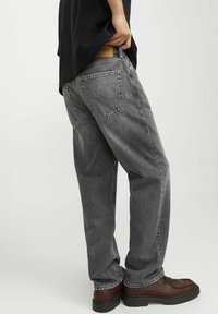 Grå denimjeans med lös passform, synliga bakfickor och en läderlapp på midjan. Kombinerat med bruna avslappnade skor.