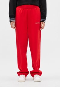 Czerwone dresy wykonane z gładkiego materiału o luźnym kroju. Posiadają haftowane logo 'Calvin Klein' w białym kolorze na lewym udzie.