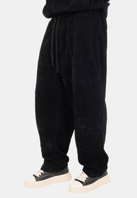 Pantaloni in corduroy neri con vita elastica e stringhe. Stile morbido e texture a coste. Abbinati a sneaker chunky bianche e nere.