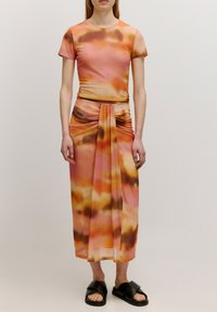 Zweiteiliges Outfit mit einem taillierten Kurzarmoberteil und einem fließenden Maxikleid. Der Stoff ist durchsichtig und zeigt ein wellenförmiges abstraktes Muster in Orange- und Brauntönen.