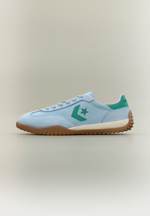 Lyseblå sneaker med grønt stjernelogo, grønn hælkappe, beige mellomsåle og brun teksturert såle, vist i profil på beige bakgrunn.