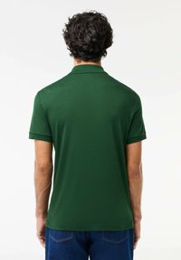 Polohemd in donkergroen, korte mouwen, gladde textuur, met een kraag en een rechte zoom. Achteraan is het ontwerp eenvoudig, zonder patronen of hardware.