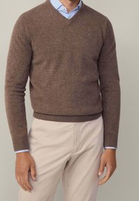 Brauner, gestrickter V-Ausschnitt-Pullover aus weichem Material. Hat lange Ärmel und ein enganliegendes Design, kombiniert mit hellen Hosen.
