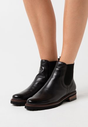 Black leather chelsea boots with elastic side panels, smooth texture, rounded toe, contrasting brown sole, and ribbed accents on the sides.