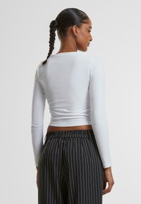 Weißes Langarmshirt mit rundem Ausschnitt, figurbetontem Design und glatter Textur, kombiniert mit schwarzen gestreiften Hosen mit elastischem Bund.