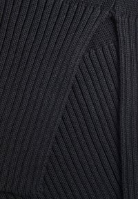 Tissu noir tricoté présentant une texture côtelée verticale marquée, avec des sections contrastantes mettant en avant des formes et des points bien définis.