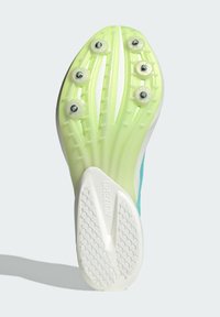 Sole di scarpa da corsa verde e bianca con sei punte metalliche, superficie di presa testurizzata e scanalature di trazione rialzate per stabilità.