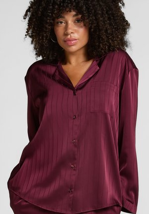 Bordeaux satijnen blouse met verticale strepen, lange mouwen, een kraag en een enkele borstzak. Voorzien van een knoopsluiting aan de voorkant.