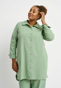 Green button-up shirt with a collar, long sleeves rolled at the cuffs, featuring a relaxed fit and soft, textured fabric.
