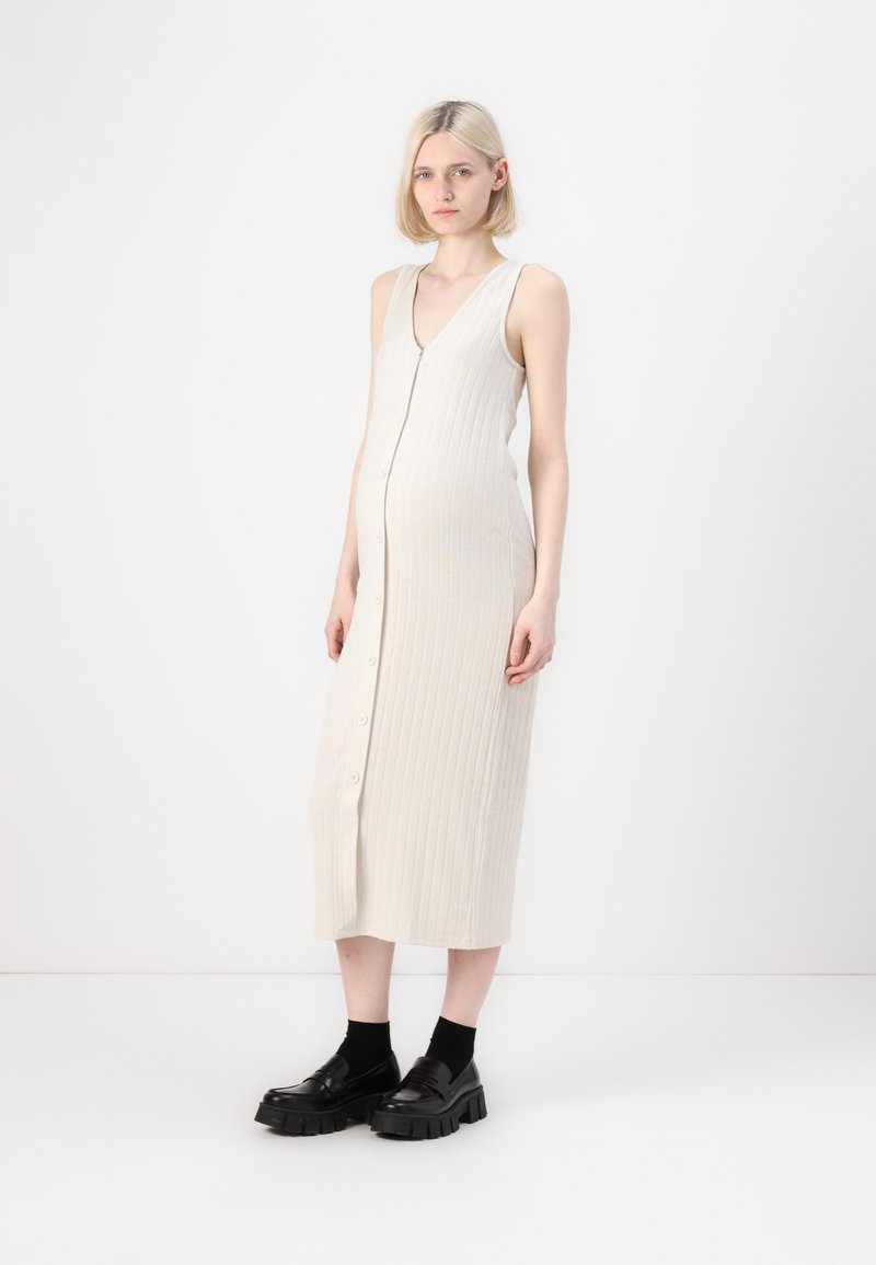 Rochie midi de culoare bej deschis, cu detaliu texturat, decolteu în V și închidere cu nasturi în față. Asortată cu mocasini negri masivi și șosete până la glezne.