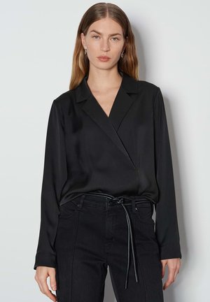 Zwarte wikkelblouse van satijnen stof met lange mouwen en een gelapte kraag, gecombineerd met hoge zwarte jeans met een strikceintuur.