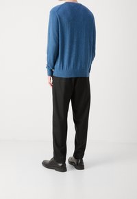 Niebieski sweter dzianinowy w cętkowany wzór, z okrągłym dekoltem i prążkowanym ściągaczem, zestawiony z czarnymi spodniami i błyszczącymi czarnymi butami.