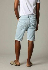 Shorts en denim bleu clair avec des revers, comportant deux poches arrière et une petite étiquette de marque sur la taille. Texture lisse.