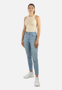 Beige ärmelloses Oberteil kombiniert mit hellblauen Skinny Jeans. Das Outfit wird durch weiße Sportsneaker ergänzt. Einfaches Design, figurbetonte Silhouette.