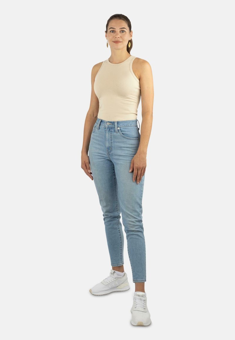 Beige ärmelloses Oberteil kombiniert mit hellblauen Skinny Jeans. Das Outfit wird durch weiße Sportsneaker ergänzt. Einfaches Design, figurbetonte Silhouette.