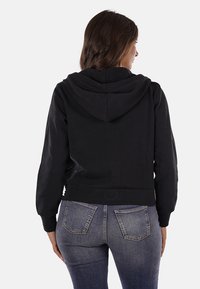 Felpa nera cropped con cappuccio, caratterizzata da una texture liscia e una silhouette aderente. Indossata con jeans in denim blu scuro.