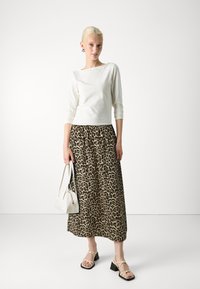 Haut à manches longues blanc, jupe maxi imprimé léopard, sandales à talons carrés beiges et petit sac à main blanc. Textures lisses et motifs audacieux.