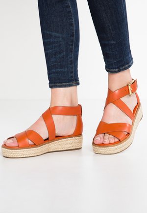 Orange lædersandaler med krydsede remme og en spændeankelrem, udstyret med en jute-indpakket hæl og åbent tådesign.
