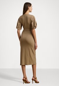 Abito midi khaki con maniche corte a sbuffo, vita aderente e texture morbida, abbinato a sandali con tacco marroni. Design minimalista, colore neutro.