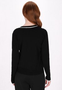 Pulover negru cu mâneci lungi, cu accente albe la gât și manșete. Țesătură moale, texturată, design ajustat și detalii cu margine dintr-un material cu striații.