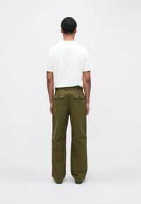 Λευκό t-shirt με στρογγυλή λαιμόκοψη, σε συνδυασμό με χακί φαρδιά παντελόνια με τσέπες στο πίσω μέρος και εμφανείς ραφές.