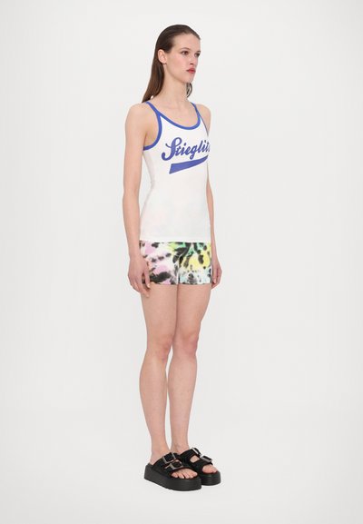 Valge tank top siniste aktsentidega ja skriptilogo, mis on ühendatud värvikirevate tie-dye šortsidega. Mustad platvorm sandaalid lõpetavad riietuse.
