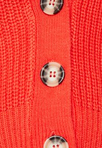 Buttoned cardigan made of textured knit fabric in bright orange, featuring three round black-and-white buttons along the front.