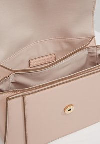 Borsa in ecopelle rosa con una superficie liscia, caratterizzata da una tasca interna. Il dettaglio con chiusura circolare dorata arricchisce il design.