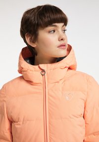 Giubbotto imbottito di colore corallo con colletto alto, caratterizzato da una zip a forma di cuore e un piccolo logo ricamato sul petto.
