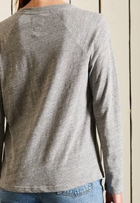 Harmaa pitkähihaisen paita, jossa on ribbaus kauluksessa ja raglan-hihat, valmistettu pehmeästä, tekstuurillisesta kankaasta, yhdistettynä farkkuihin.
