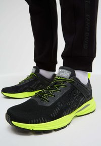 Black athletic shoes with neon green accents, mesh upper, textured pattern, cushioned sole, and logo on the side and tongue.