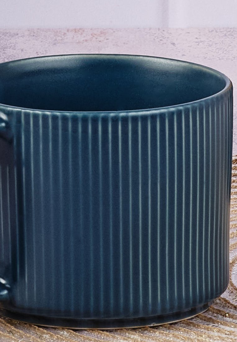 Dunkelblaue Keramiktasse mit vertikalen Rillen an der Außenseite, auf einer gewebten Oberfläche platziert.