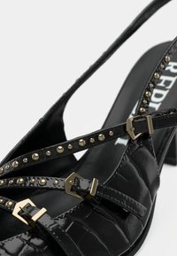 Sandal in vernice nera con texture in coccodrillo, dotato di dettagli in metallo dorato e cinturini alla caviglia regolabili su un tacco a blocco.