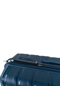 Maleta rígida azul oscuro con rayas texturizadas, que cuenta con una cremallera, un mecanismo de bloqueo y puertos eléctricos en el lateral.