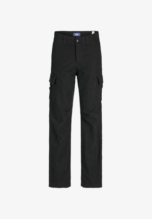 Osoba ubrana w czarną bluzę Jack & Jones, ciemne spodnie typu cargo oraz brązowe trampki z białymi paskami stoi na jednolitym jasnym tle.